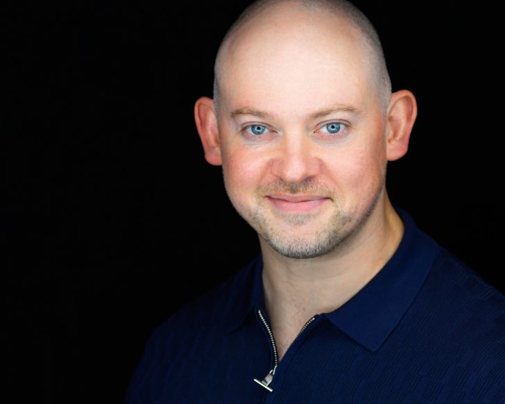 Smiling man in blue shirt against black background.
