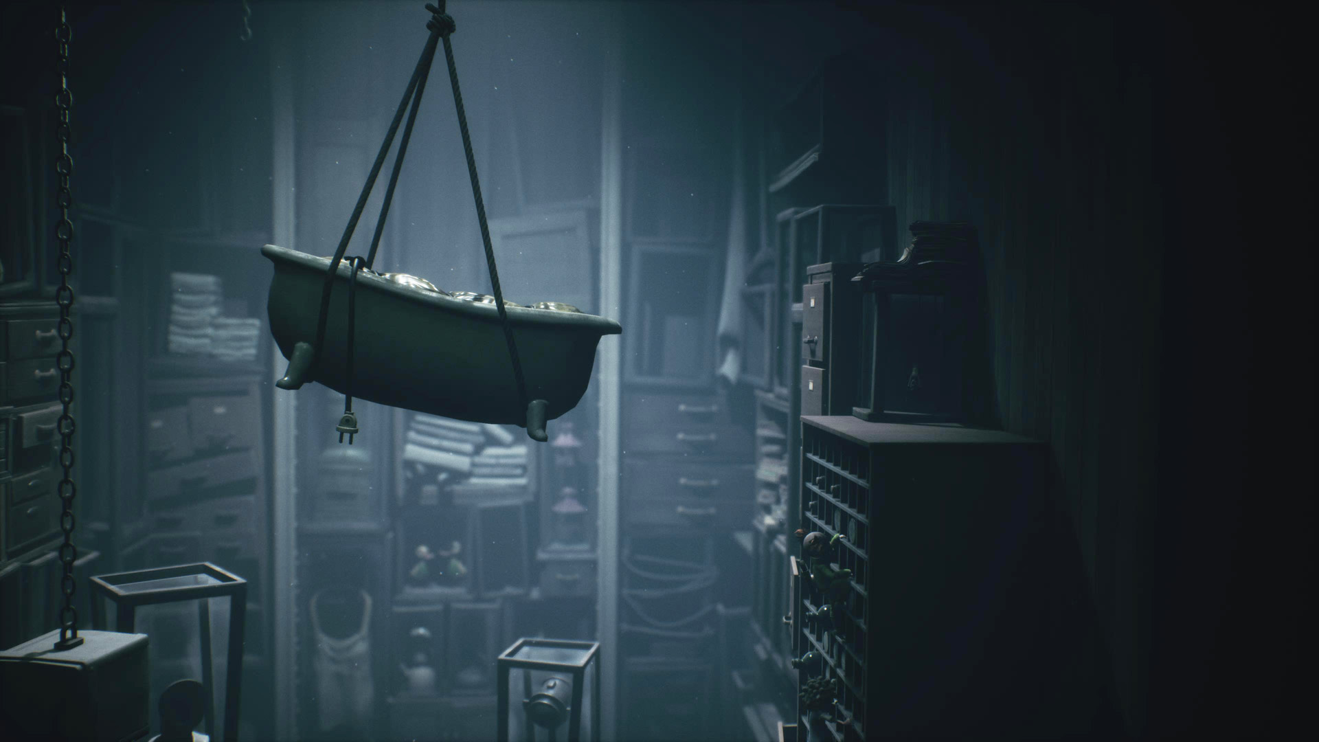 A suspended bathtub hangs in a dimly lit room filled with storage boxes and cabinets.